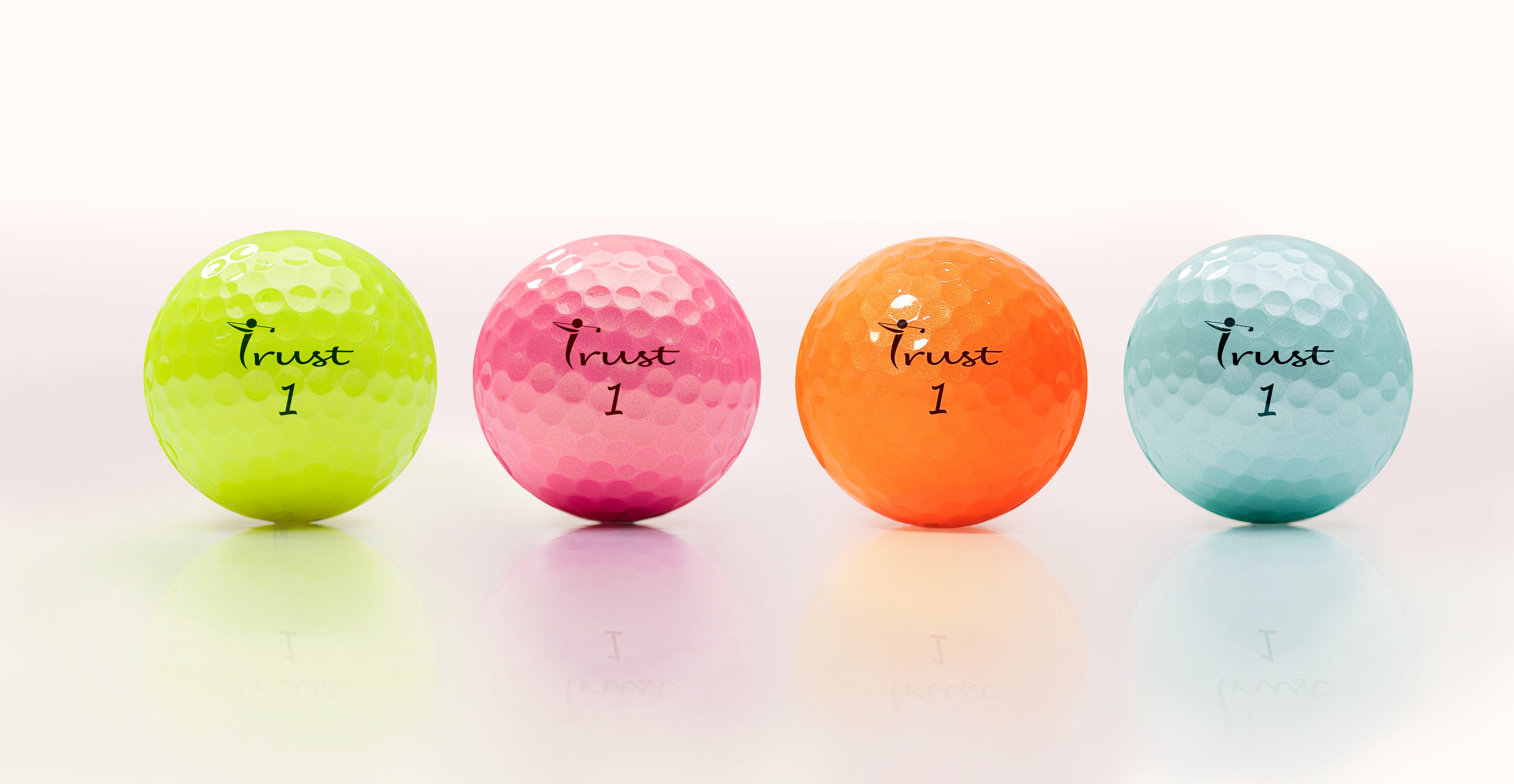 Four colorful golf balls with 'Trust 1' text on a white background. Available color: yellow, pink, orange, blue.